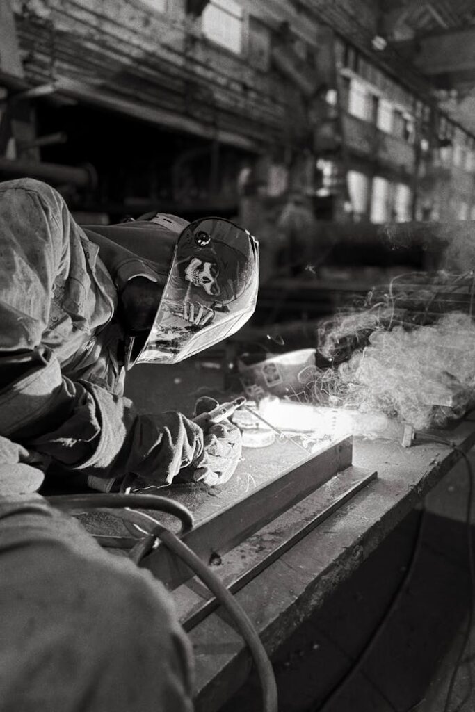 pexels photo 34040513 Black and white photo of a welder working in an industrial setting, wearing protective gear.