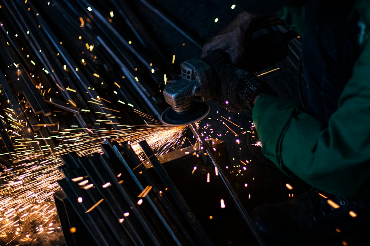 Offerings A worker using a grinder on metal, creating bright sparks in a dark workshop setting.